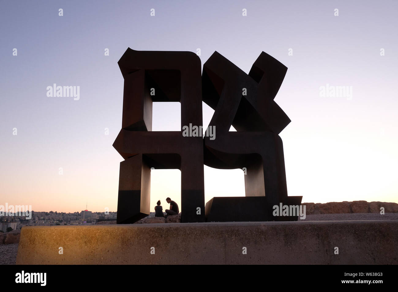 A couple sitting next to the Ahava ( Love ) sculpture by Robert Indiana 1977 depicting Hebrew letters forming that word on display in the Billy Rose art garden of Israel Museum, Jerusalem Stock Photo