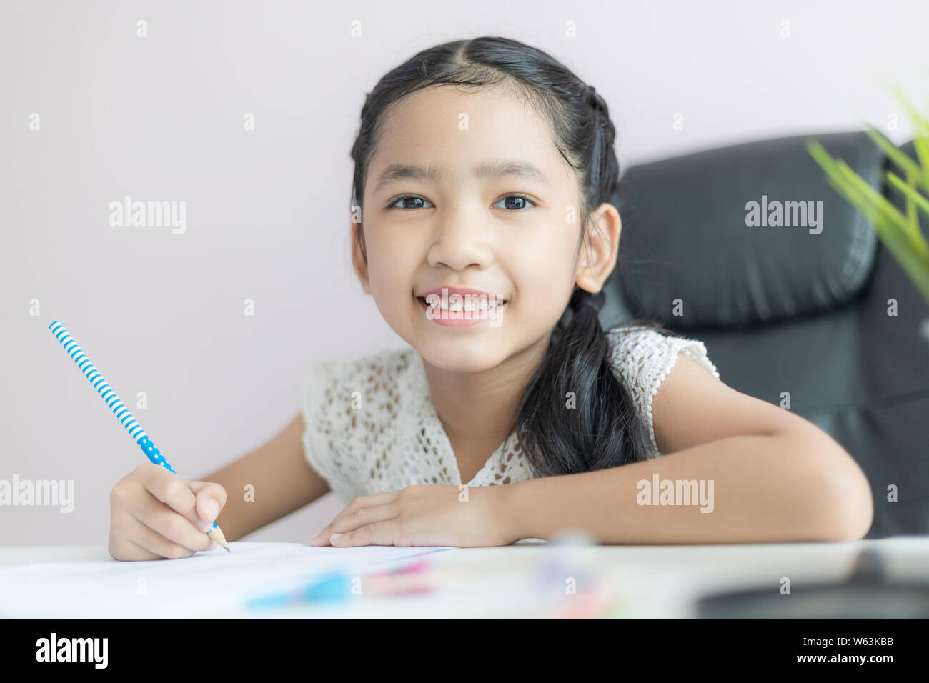 Little Asian girl using the pencil to write on the paper doing homework and...