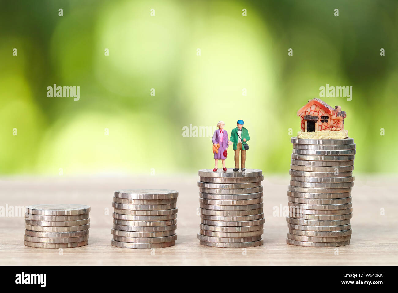 miniature old couple standing on stack coins with house and green background (idea for saving money after retire) Stock Photo