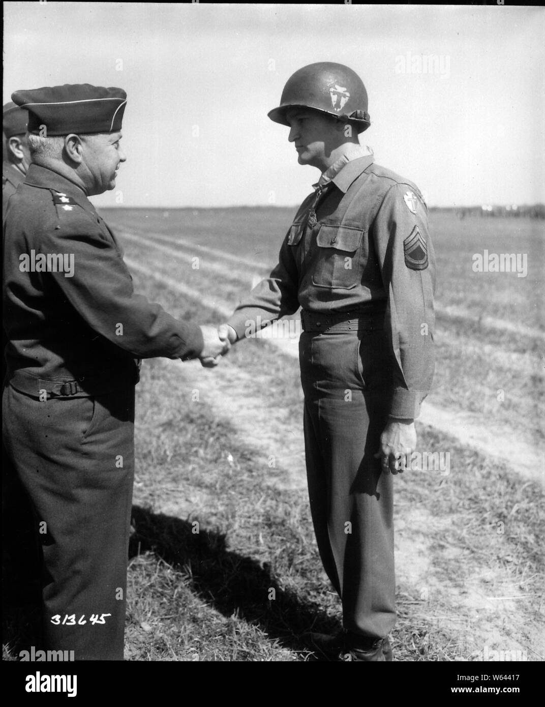 T/Sgt. Charles H. Coolidge, Signal Mountain, Tenn., a member of Co. M 141st infantry 36th infantry, VI Corps, Seventh Army, is congratulated by Lt. Gen Wade H. Haislip, CG US Seventh Army, after he was presented with the Congressional Medal of Honor, for meritorious service in leading a section of heavy machine gunners who took and held a position east of Belmont Sur Buttant, France until it was apparent that the position could no longer be defended, and in the meantime the section covered the right flank of the 3rd Bn. and supported its action. 18th June 1945. Dornandt, Germany. Stock Photo