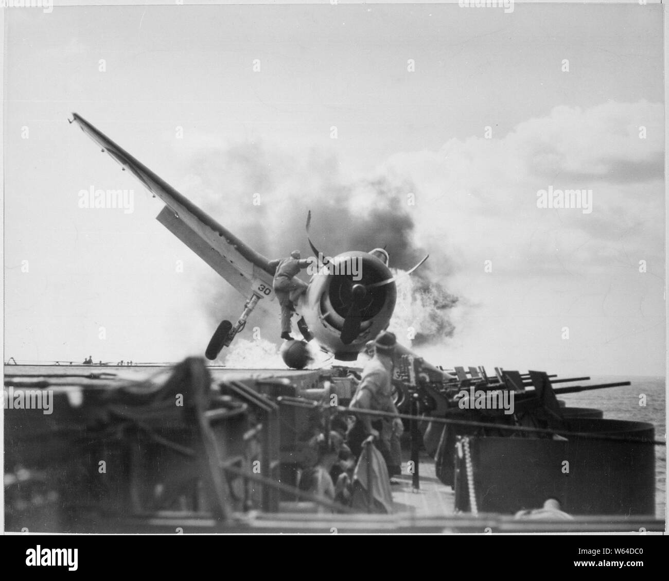 Crash landing of F6F on flight deck of USS ENTERPRISE while enroute to attack Makin Island. Lieutenant Walter Chewning, catapult officer, clambering up the side of the plane to assist pilot, Ens. Byron Johnson, from the flaming cockpit.; General notes:  Use War and Conflict Number 964 when ordering a reproduction or requesting information about this image. Stock Photo