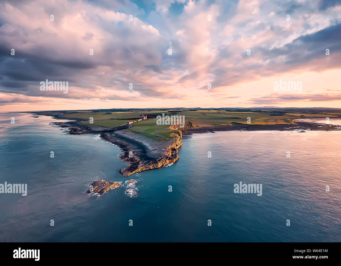 View from above on Embleton bay, North sea, the cliff with seagulls, ruins and green agricultural fields. Sunset. England countryside. Northumberland Stock Photo