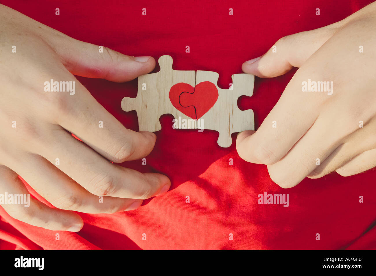 Red heart is drawn on the pieces of the puzzle in male hands on red background. Love concept. St. Valentine day Stock Photo