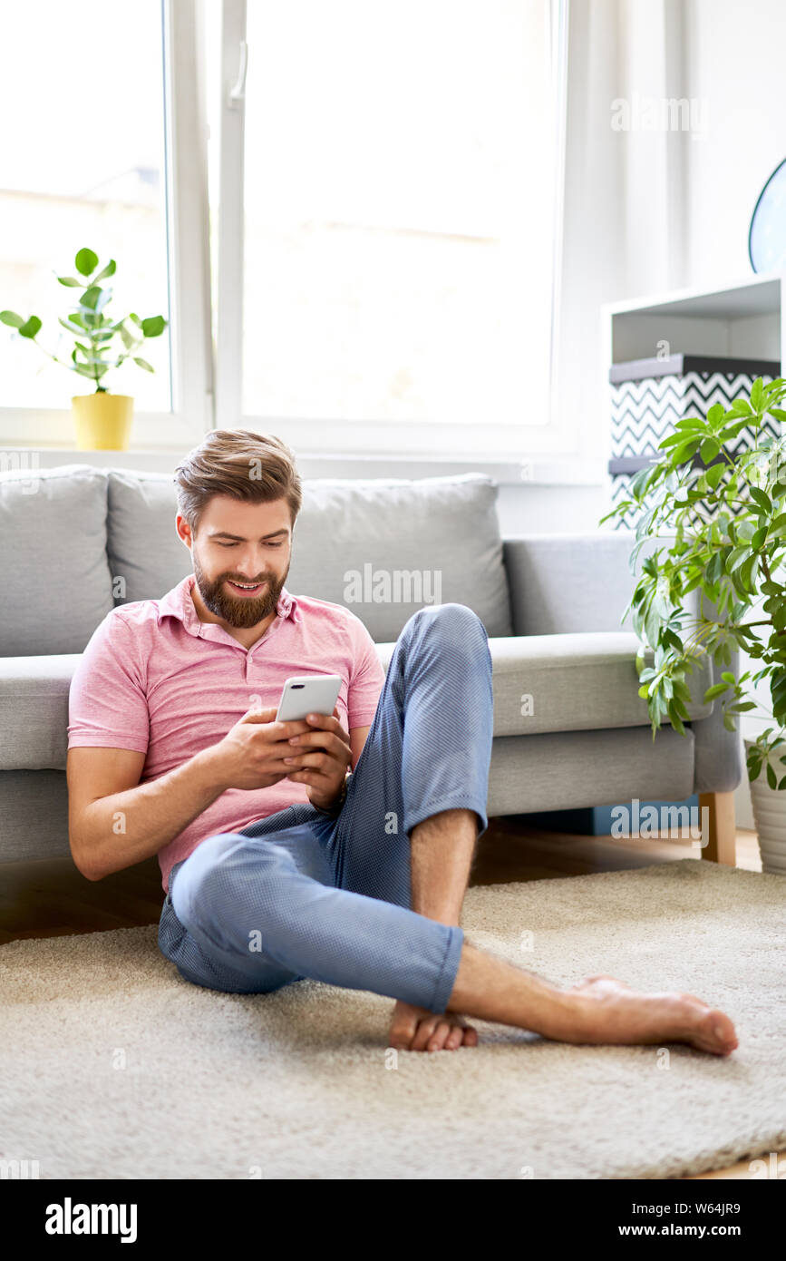 Relaxed man using phone at home sitting on the floor Stock Photo