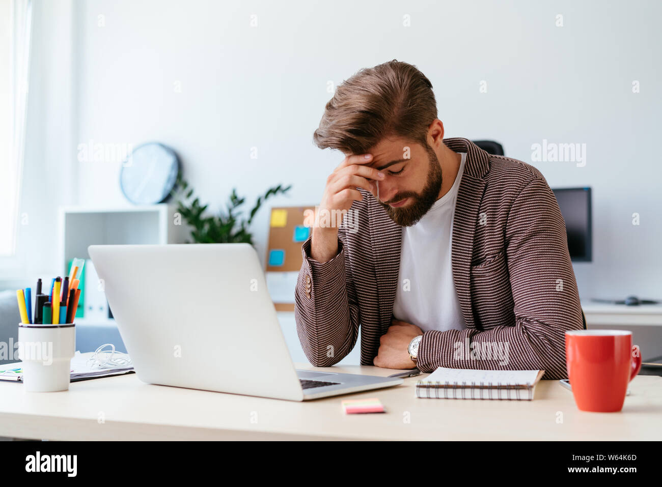 Young businessman sitting at desk and having headache while working with laptop in modern office Stock Photo