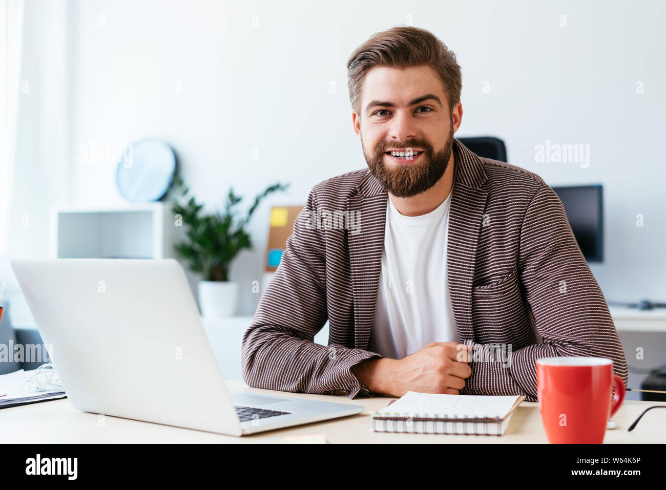 Portrait of young startup businessman sitting in small modern office and looking at camera Stock Photo