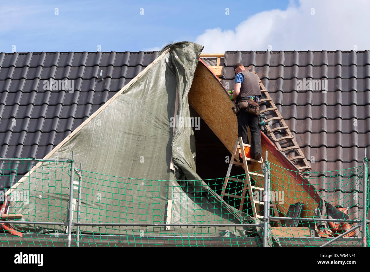Roofer stands unsecured on a ladder Stock Photo