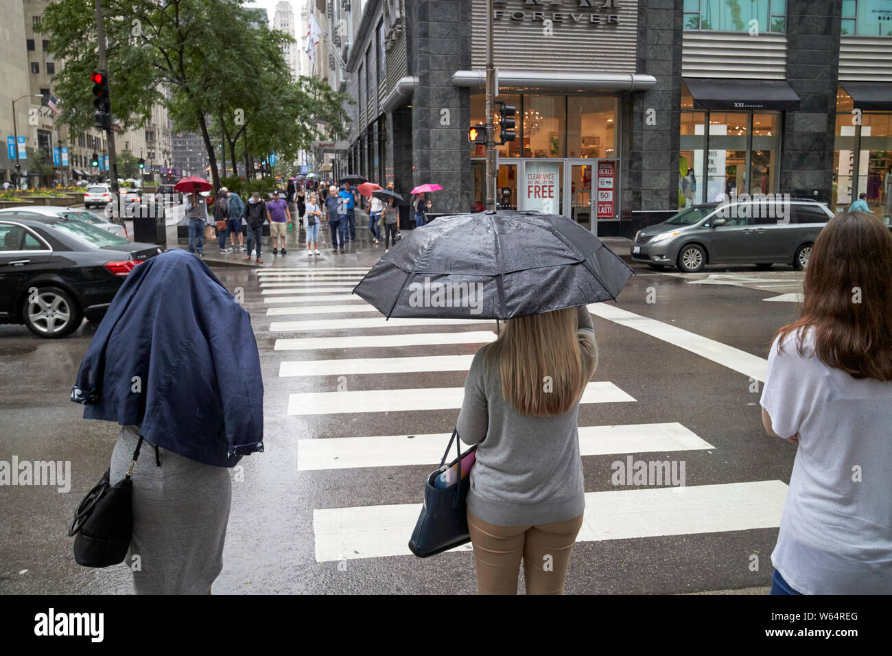 women holding umbrellas and coat over head stand at crosswalk waiting in the rain on michigan avenue downtown Chicago IL USA Stock Photo