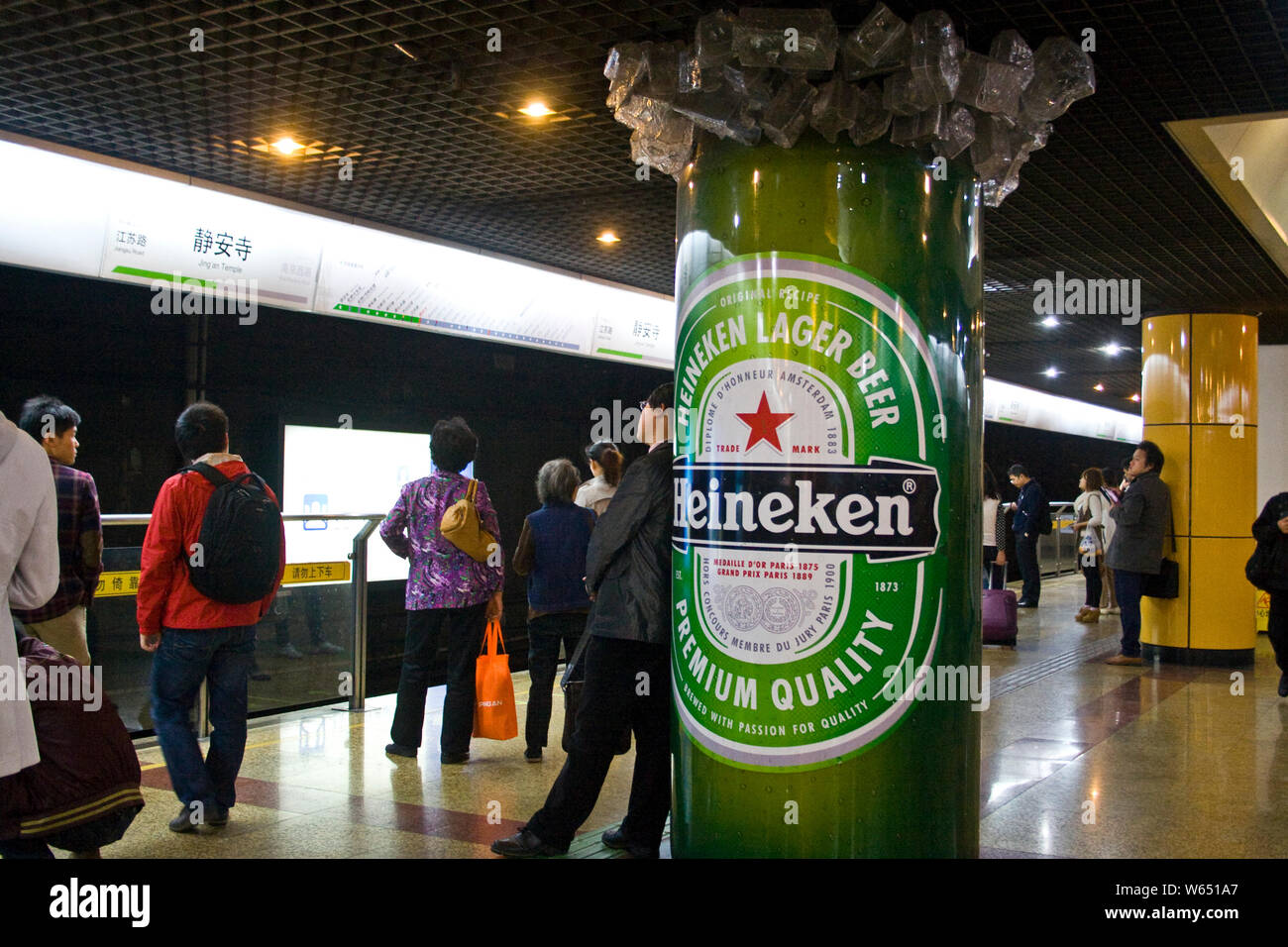 --FILE--Passengers wait for subway trains next to an advertisement for Heineken Lager Beer at a metro station in Shanghai, China, 2 November 2012.   H Stock Photo