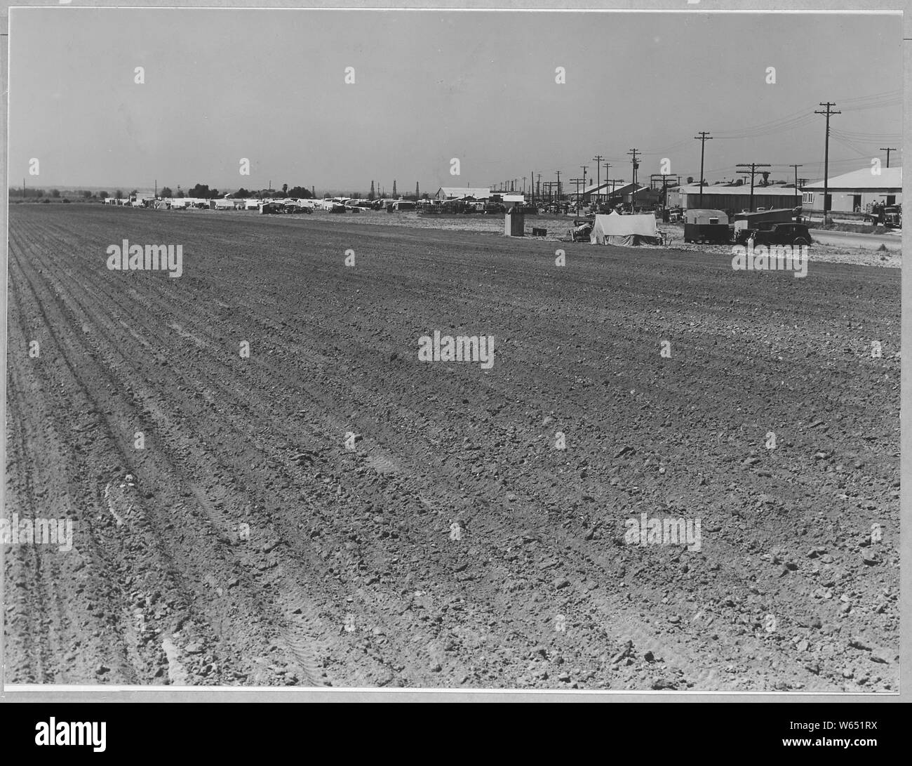 Edison, Kern County, California. The town of Edison, a potato town in a nearly developing large-scal . . .; Scope and content:  Full caption reads as follows: Edison, Kern County, California. The town of Edison, a potato town in a nearly developing large-scale potato district. Shows camp for migratory potato pickers across field of potatoes already picked. Shows packing sheds along railroad tracks. 27,250 acres of potatoes were planted in Kern County in 1940. Over 200 families encamped in tents and trailers during this potato season, but not getting much work in the fields because of locals. B Stock Photo