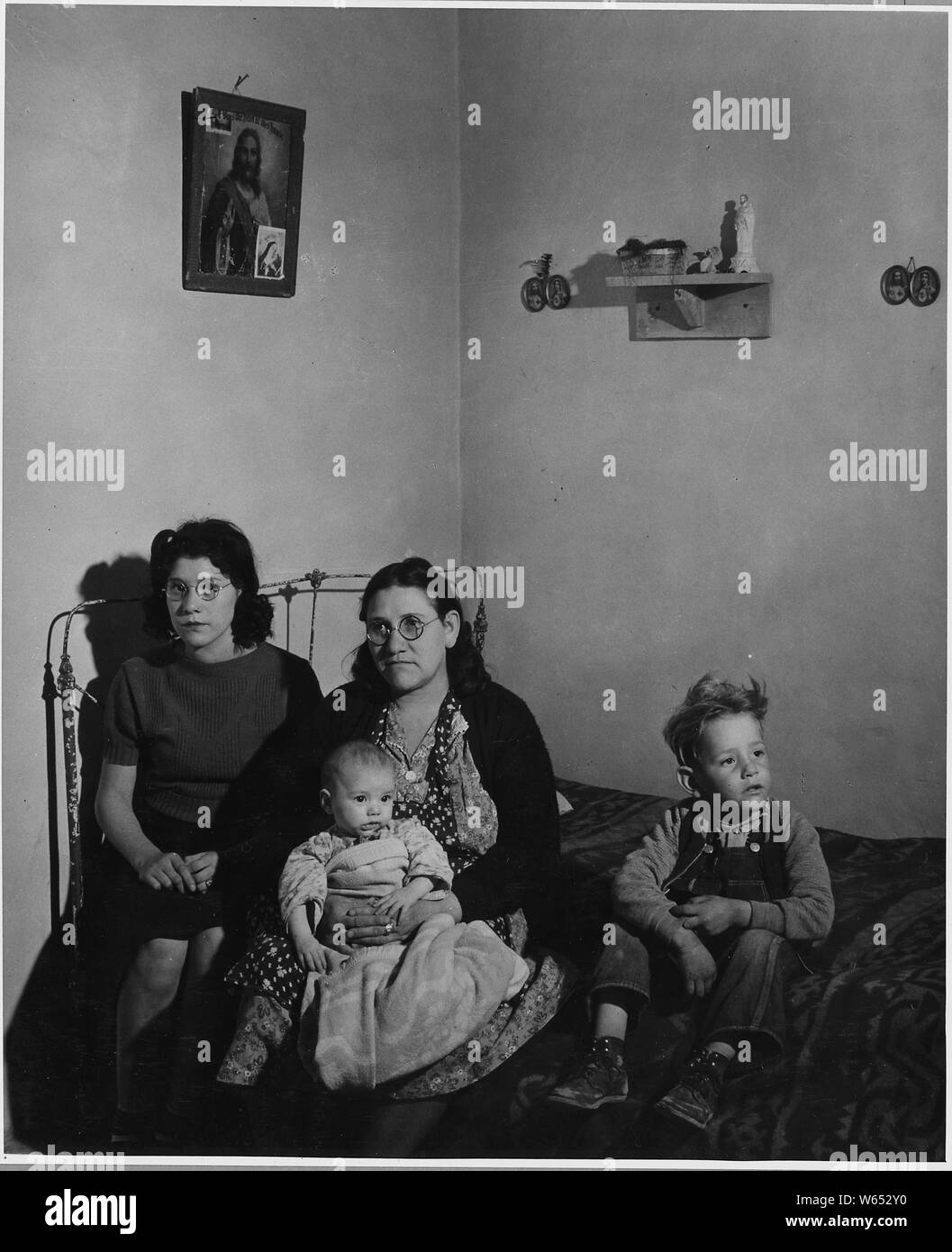 El Cerrito, San Miguel County, New Mexico. Rooms in all these houses differ considerably as to furn . . .; Scope and content:  Full caption reads as follows: El Cerrito, San Miguel County, New Mexico. Rooms in all these houses differ considerably as to furniture, arrangement and shape, but almost all of them are surprisingly clean and well kept. The influence of the church on the lives of these people is very strongly reflected in the decorating to be seen on the walls of their homes. Notice that nearly every one of these pictures shows some sort of religious symbol. Stock Photo