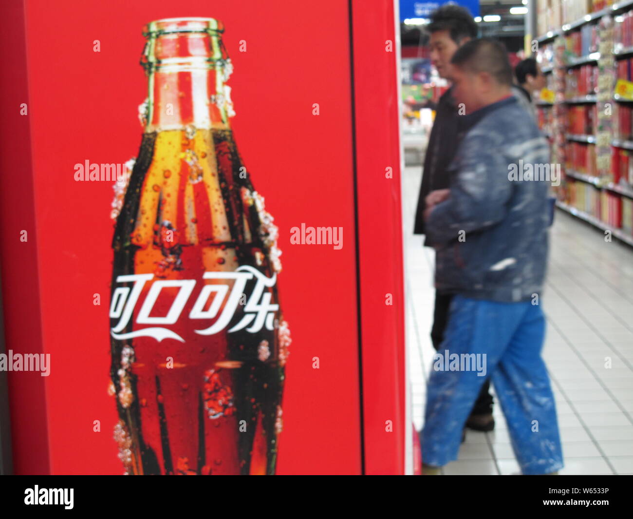 --FILE--Customers walk past an advertisement for Coca-Cola at a supermarket in Shanghai, China, 6 April 2018.   US soda and beer lovers might want to Stock Photo
