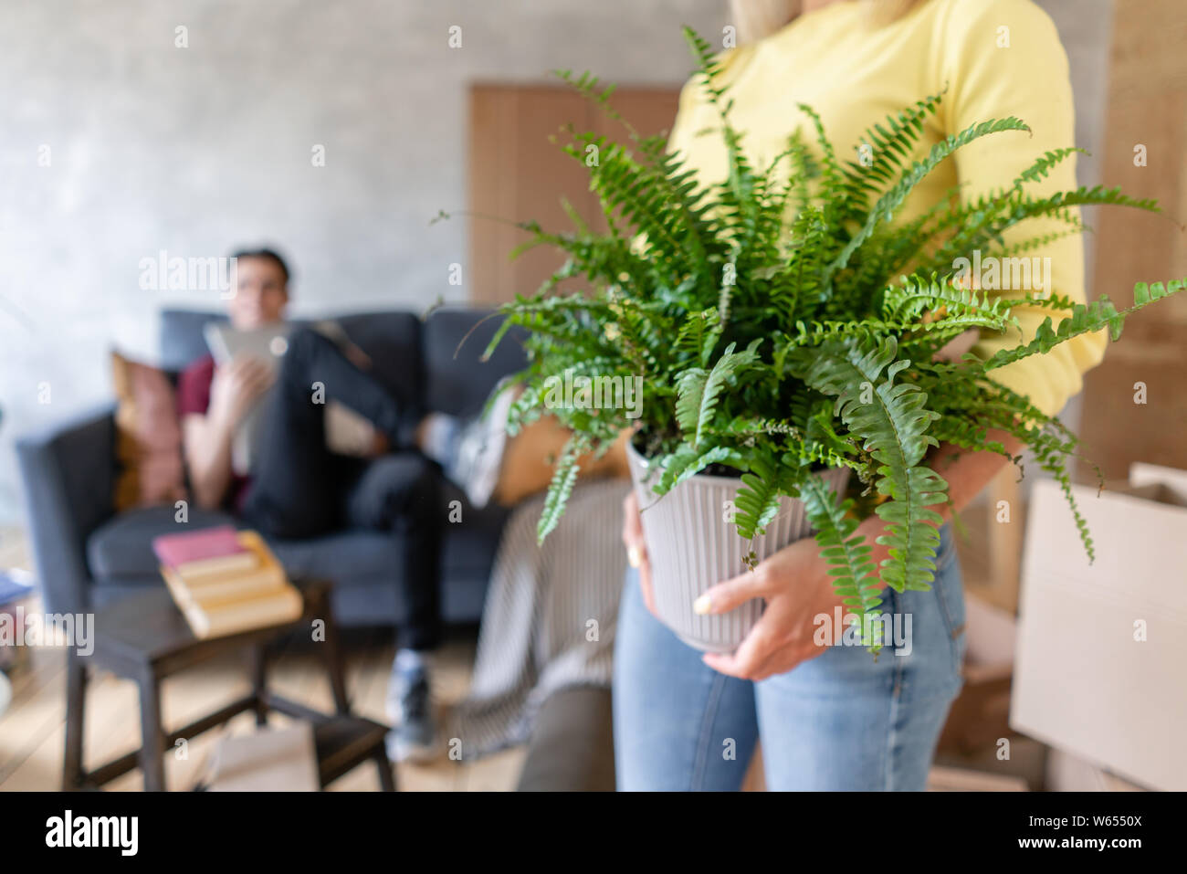 Woman in the foreground holding a fern flower in her hands. Young couple moving to a new apartment together. Relocation concept Stock Photo