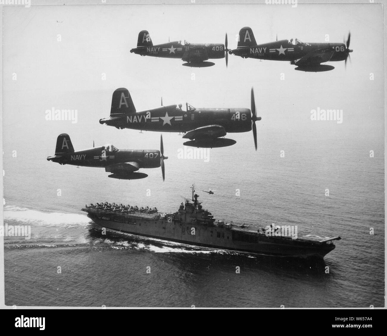 F4U's (Corsairs) returning from a combat mission over North Korea circle the USS Boxer as they wait for planes in the next strike to be launched from her flight deck-a helicopter hovers above the ship.; General notes:  Four U.S. Navy Vought F4U-4 Corsiars from fighter squadron VF-884 Bitter Birds fly past their parent carrier USS Boxer (CV-21) on 4 September 1951. Boxer was deployed to Korea with Carrier Air Group 101 (CVG-101) from 2 March to 24 October 1951. Stock Photo