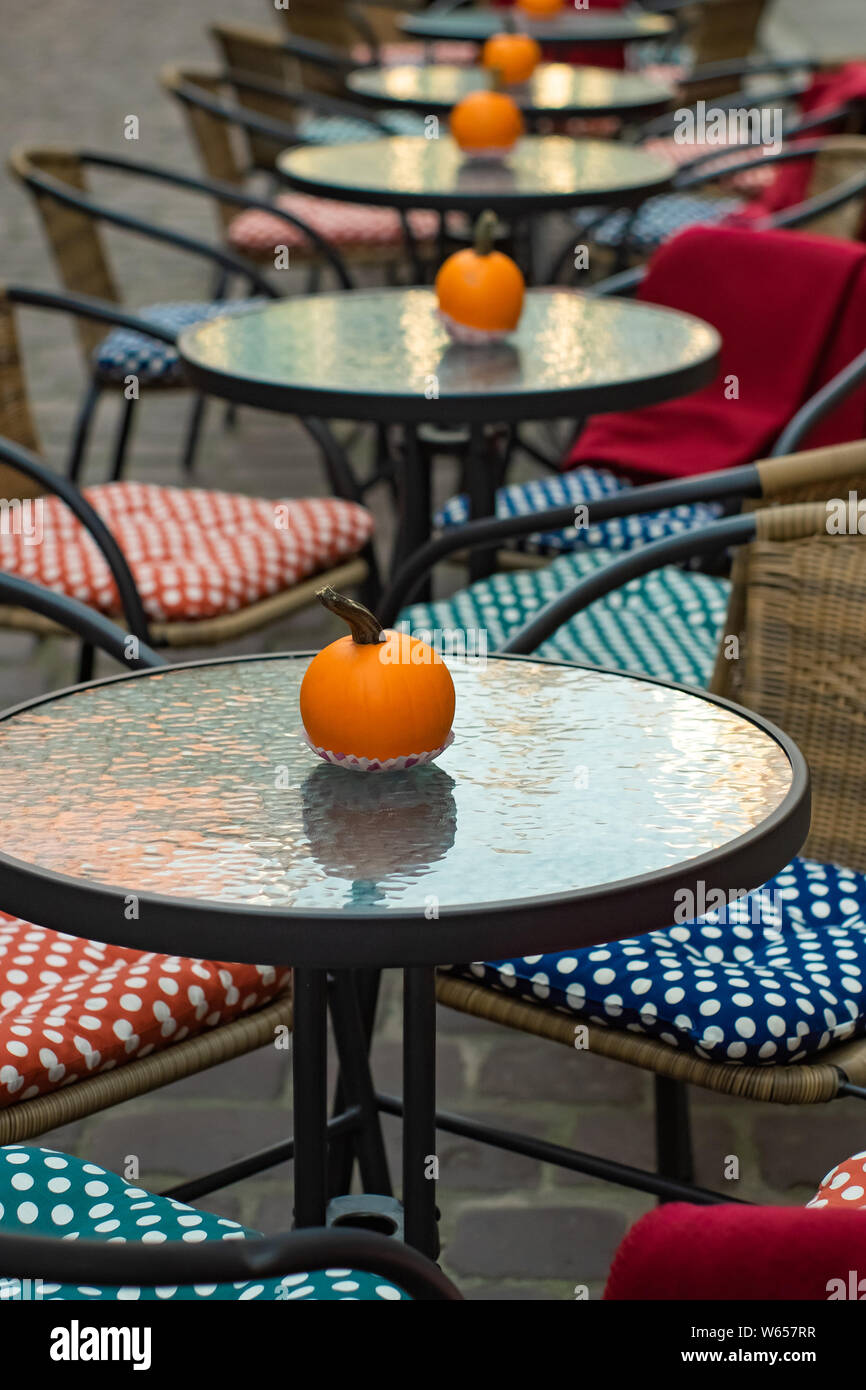 glass tables of an outdoor cafe with pumpkins and colored cushions of