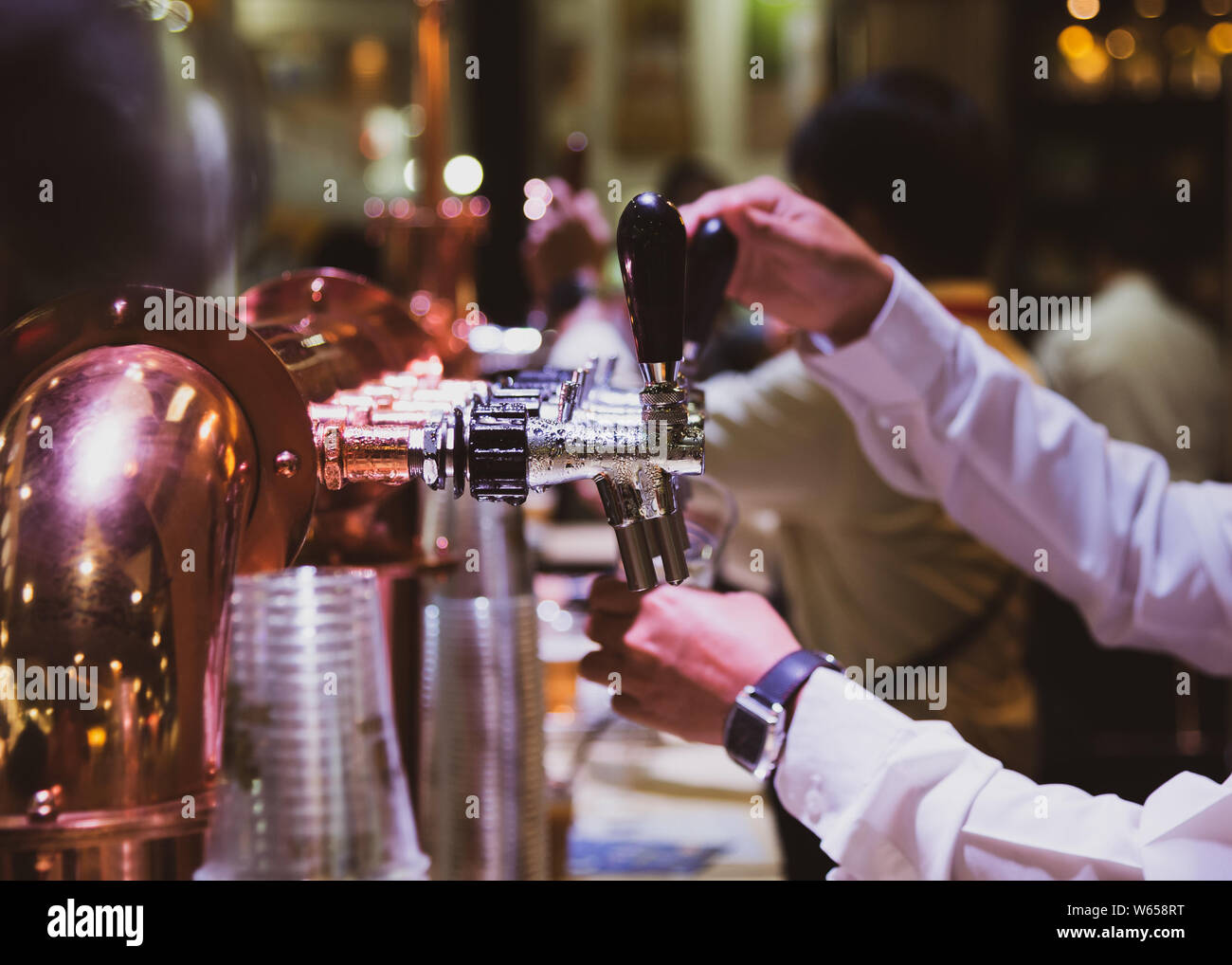Bartender pouring draft beer in the bar, Barman hand at beer tap pouring draught lager beer serving in a restaurant or pub Stock Photo