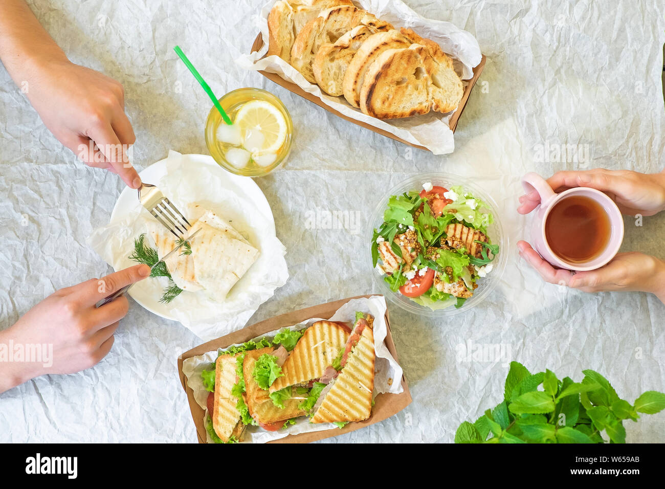 Caesar salad, bruschetta, ham and tomato sandwiches table with hands, top view from above Stock Photo