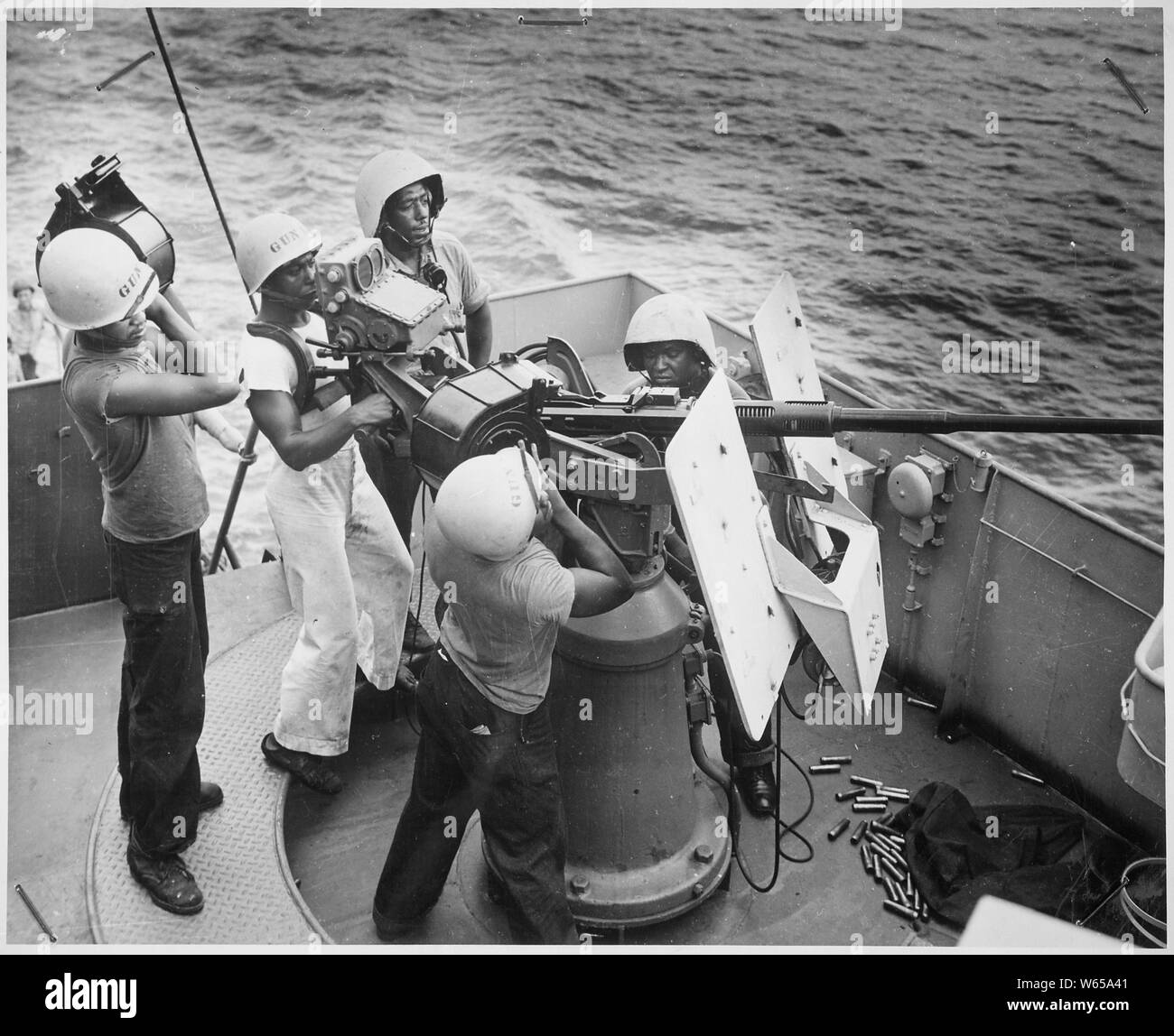 Five steward's mates stand at their battle stations, as a gun crew aboard a Coast Guard-manned frigate in the southwest Pacific. On call to general quarters, these Coast Guardsmen man a 20mm AA gun. They are, left to right, James L. Wesley, standing with a clip of shells; L. S. Haywood, firing; William Watson, reporting to bridge by phone from his gun captain's post; William Morton, loading a full clip, assisted by Odis Lane, facing camera across gun barrel., ca. 1941 - ca. 1945 Stock Photo