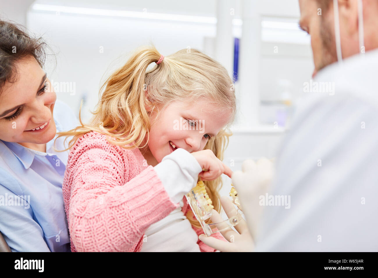 Pediatric dentist shows girl a denture model before the examination in pediatrician practice Stock Photo