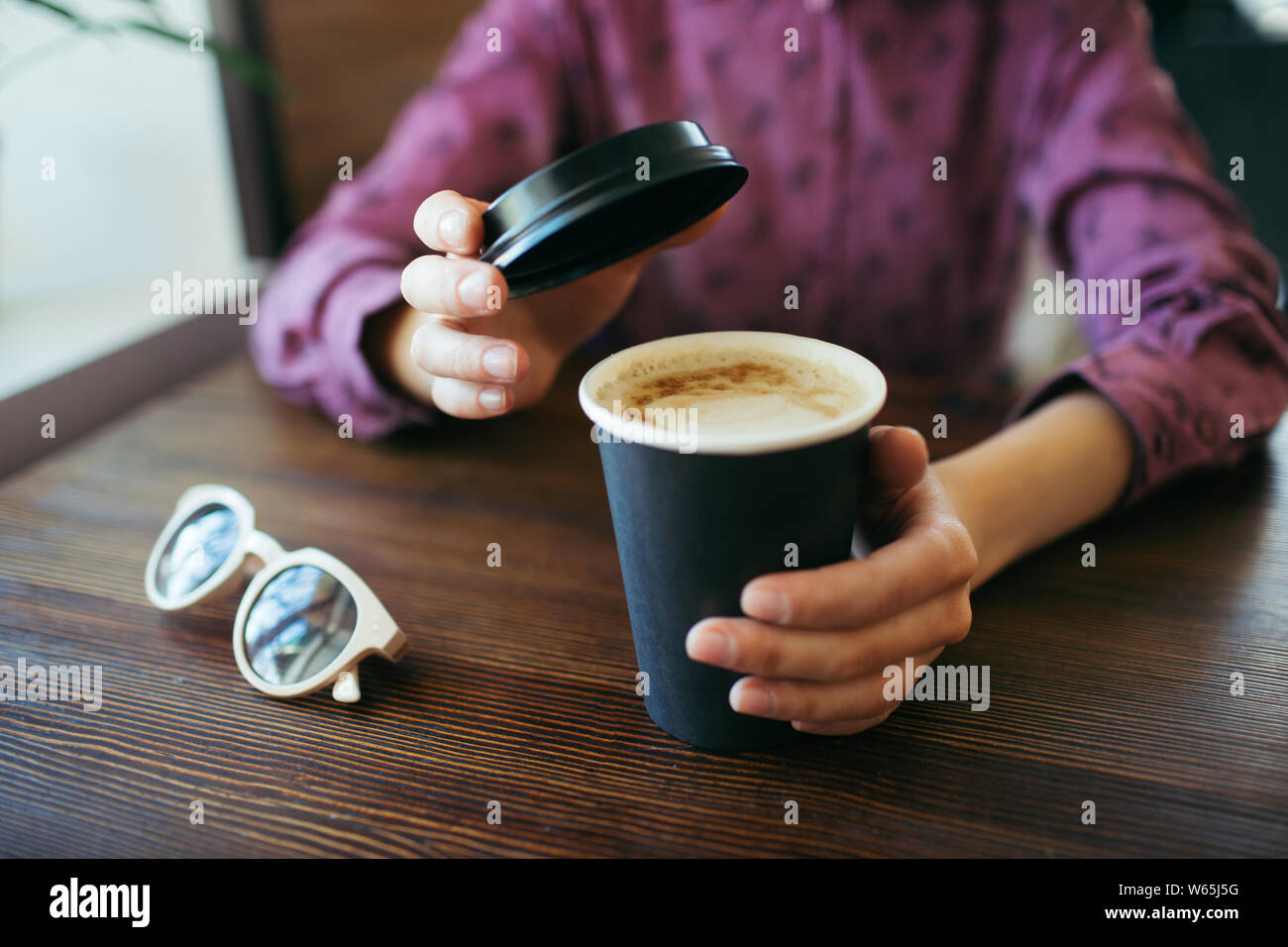 Female hands with a cup of cappuccino, with thick foam in black takeaway paper cup. Stock Photo