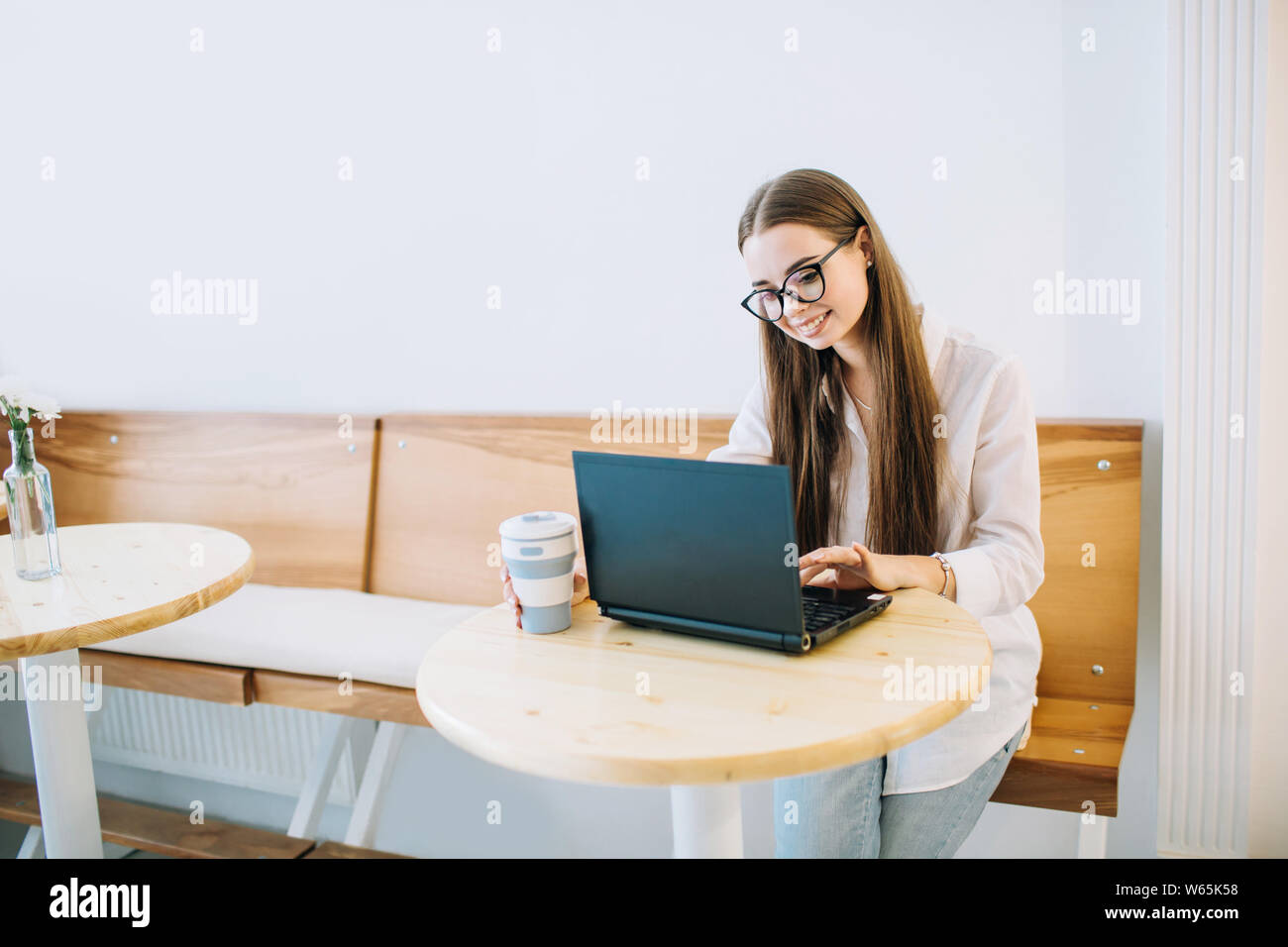 Young smiling woman working on laptop at a cafe, while drinking coffee ...