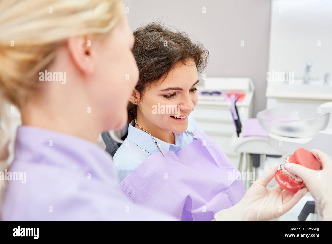 Dental assistant shows patient on a denture model the effect of the planned braces Stock Photo