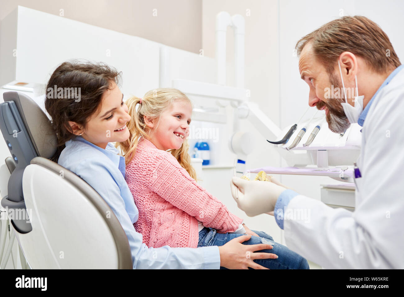 Pediatric dentist explains child on the mother's lap the planned treatment in the doctor's office Stock Photo