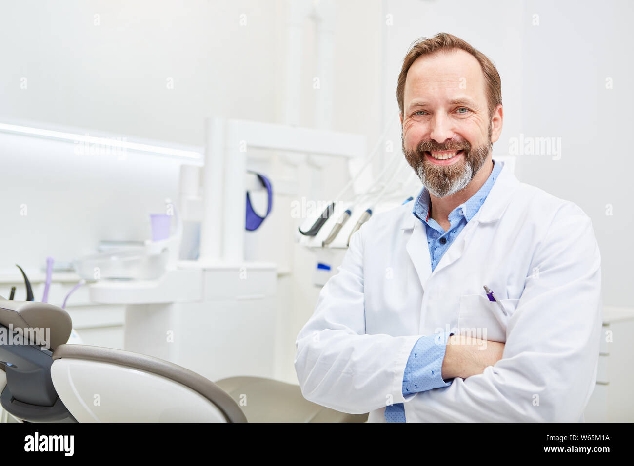 Successful dentist in white coat with arms crossed in his dental office