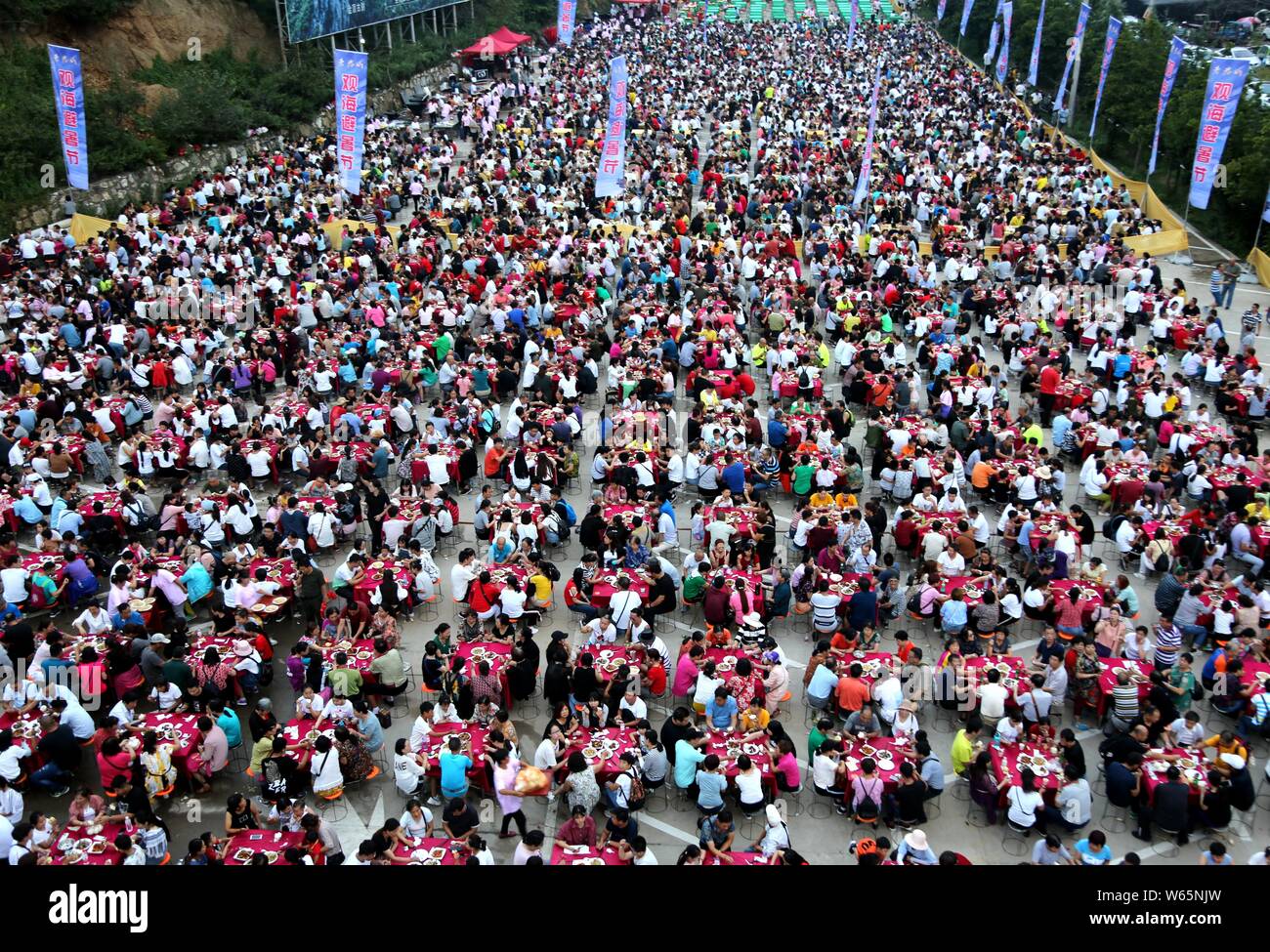 Thousands of tourists eat dinner around tables during a free-flowing banquet held at the parking lot of the Laojun Mountain scenic spot in Qiliping vi Stock Photo