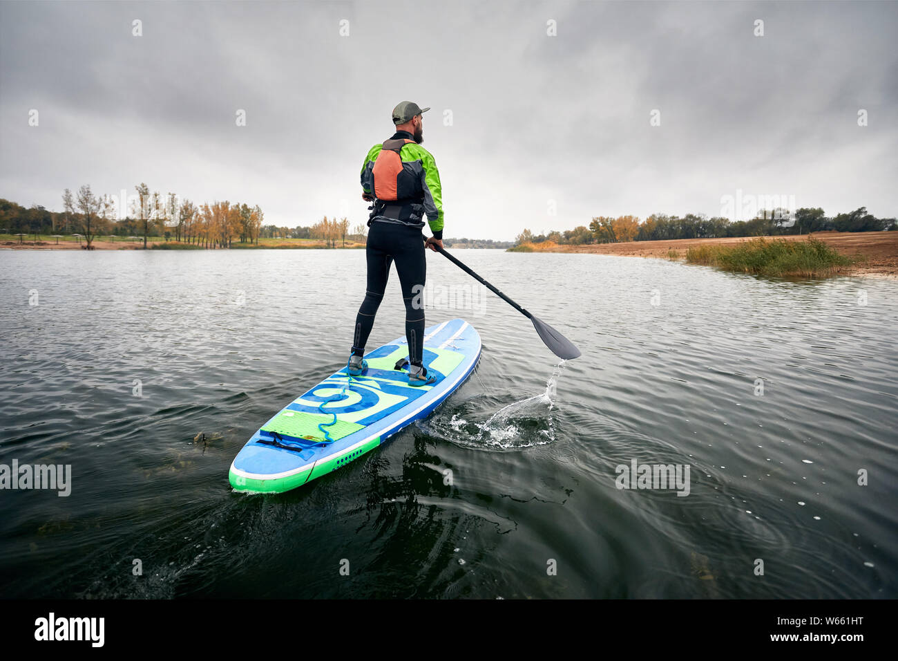 Athlete in wetsuit on paddleboard exploring the lake at cold weather