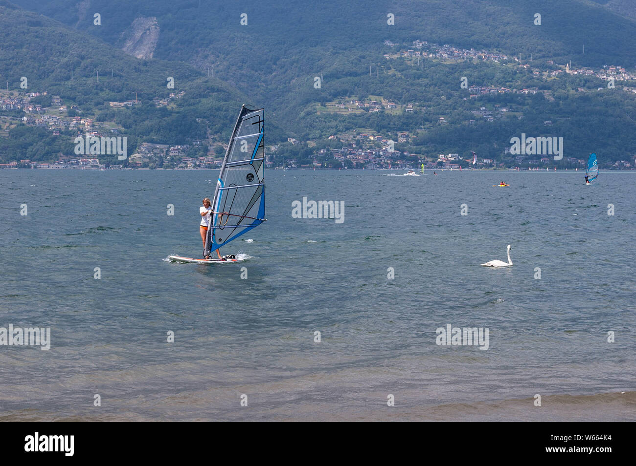 Lake Como, Italy - July 21, 2019. Water sport: woman windsurfer surfing the wind on waves on a bright sunny summer day near the Colico and swimming sw Stock Photo