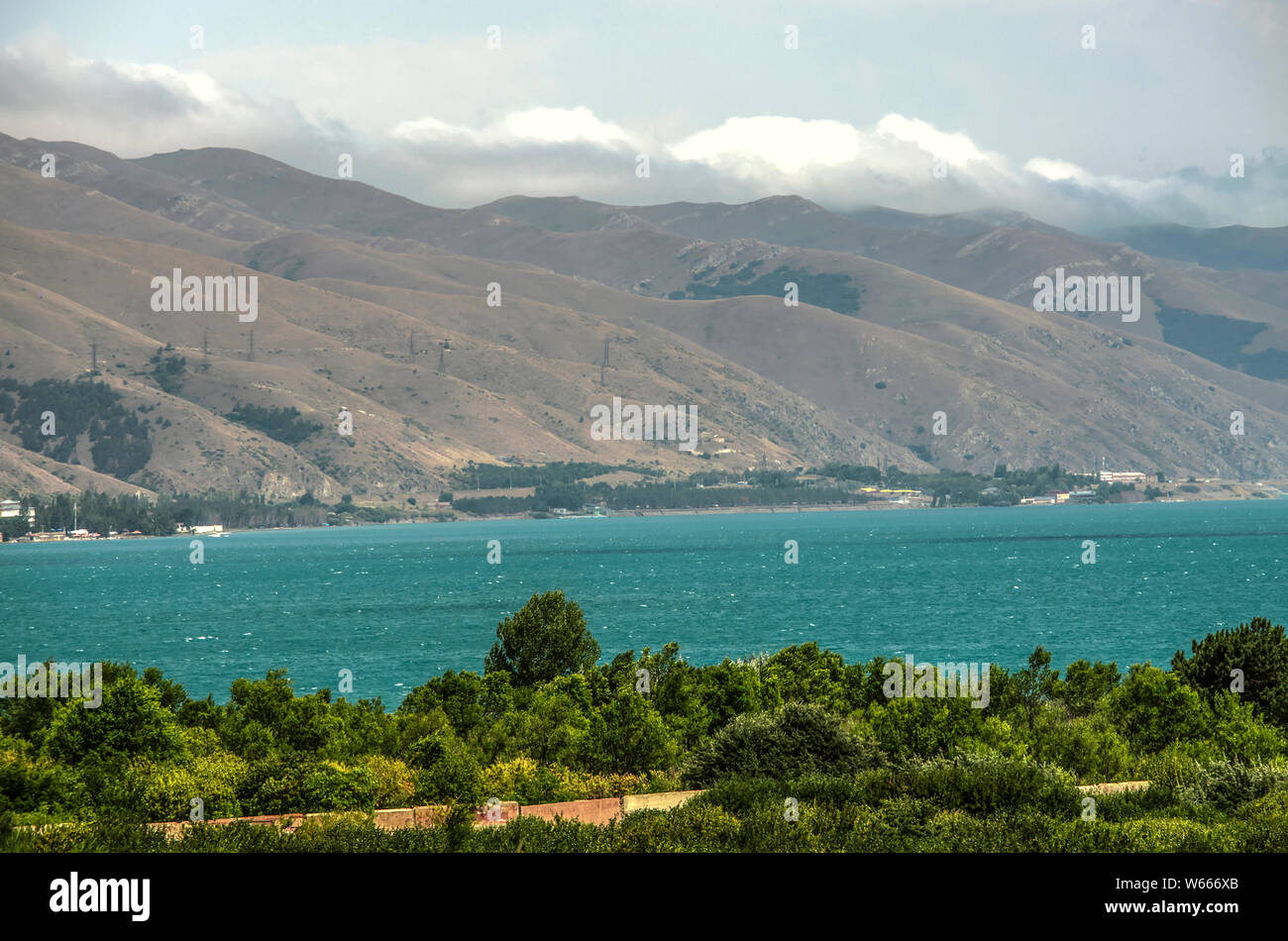 The shore of lake Sevan covered with trees and bushes surrounded by the mountains of Gegham ridge at an altitude of 1900 meters above sea level Stock Photo