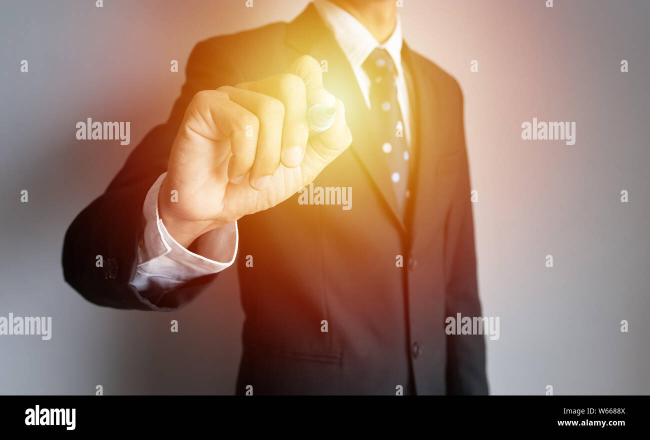 businessman hand holding black magic pen write something with virtual blank transparent whiteboard screen with copy space, light effect at pen Stock Photo