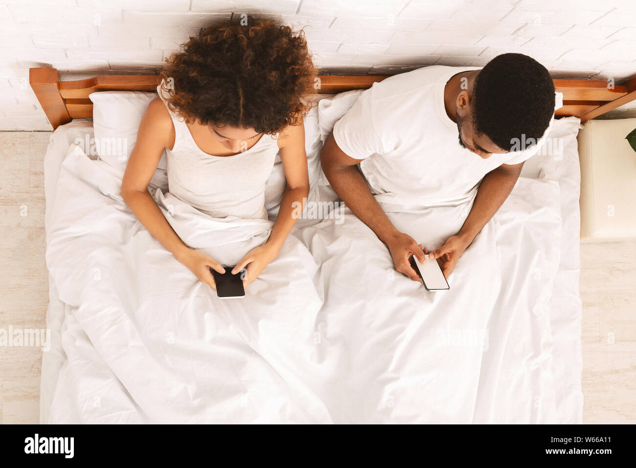 Millennial couple lying on bed back to back with smartphones Stock Photo