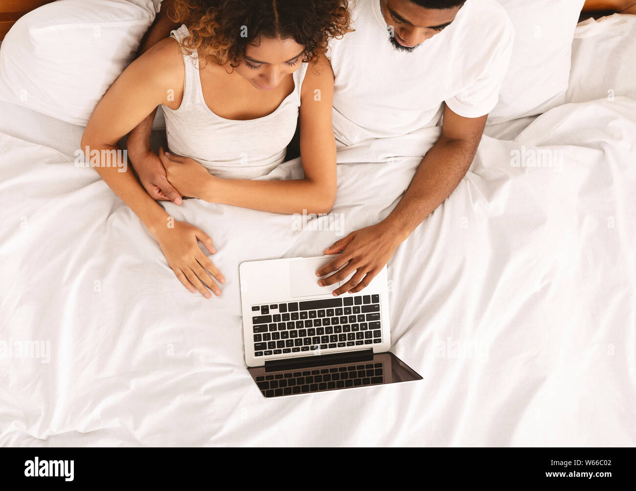 Young black couple lying on bed and using laptop Stock Photo - Alamy