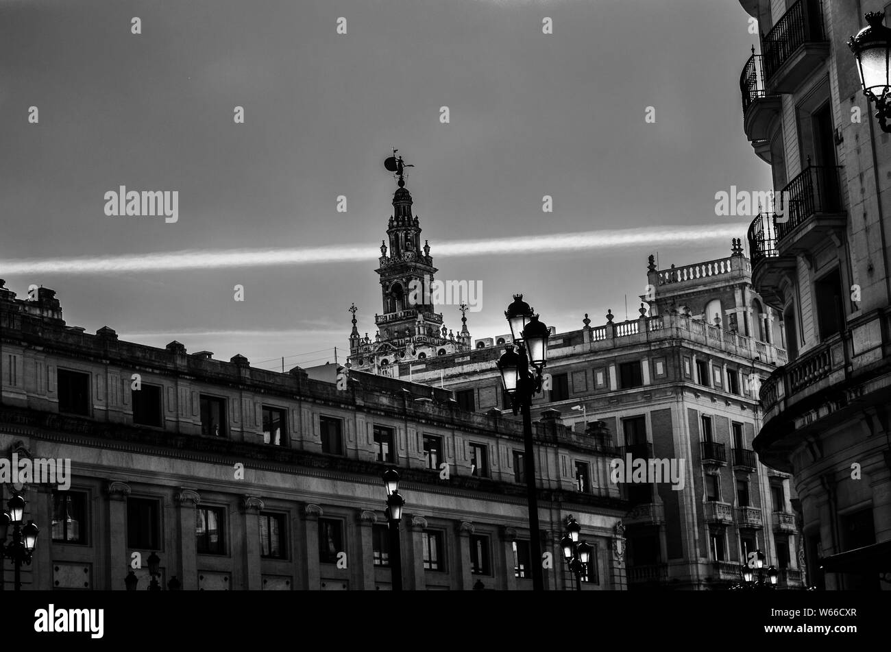 Black and white picture of a chemtrail behind the Giralda Tower in Seville, Spain Stock Photo