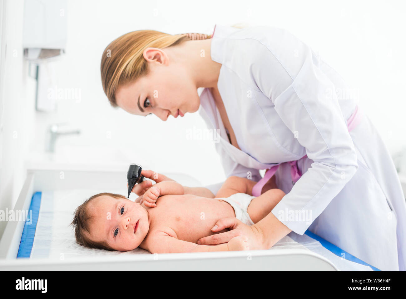 Beautiful young female blonde doctor examining little baby with ear ...