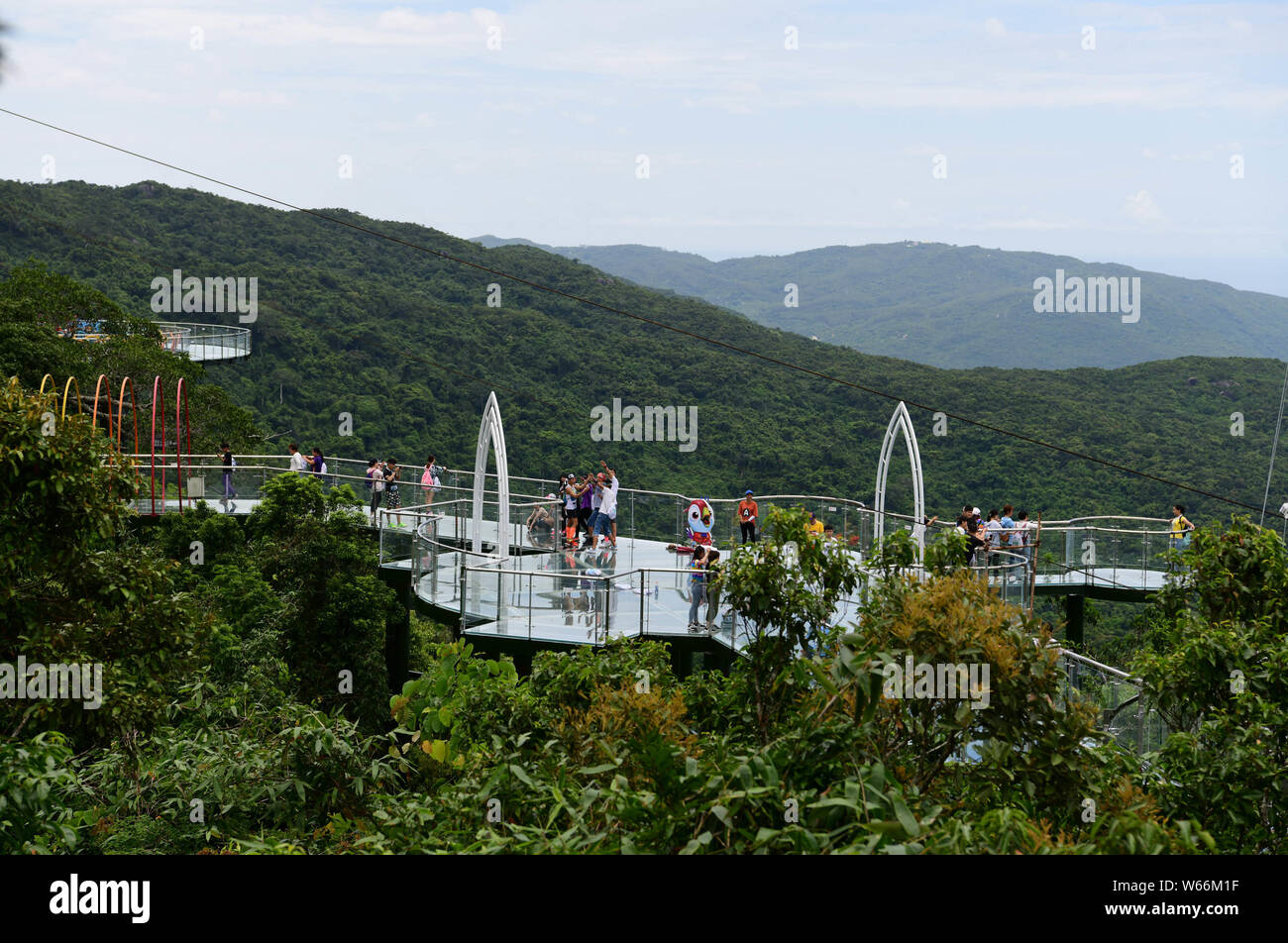 Tourists walk on a glass-bottomed sky walkway at the Yalong Bay forest park in Sanya city, south China's Hainan province, 29 July 2018.   People visit Stock Photo