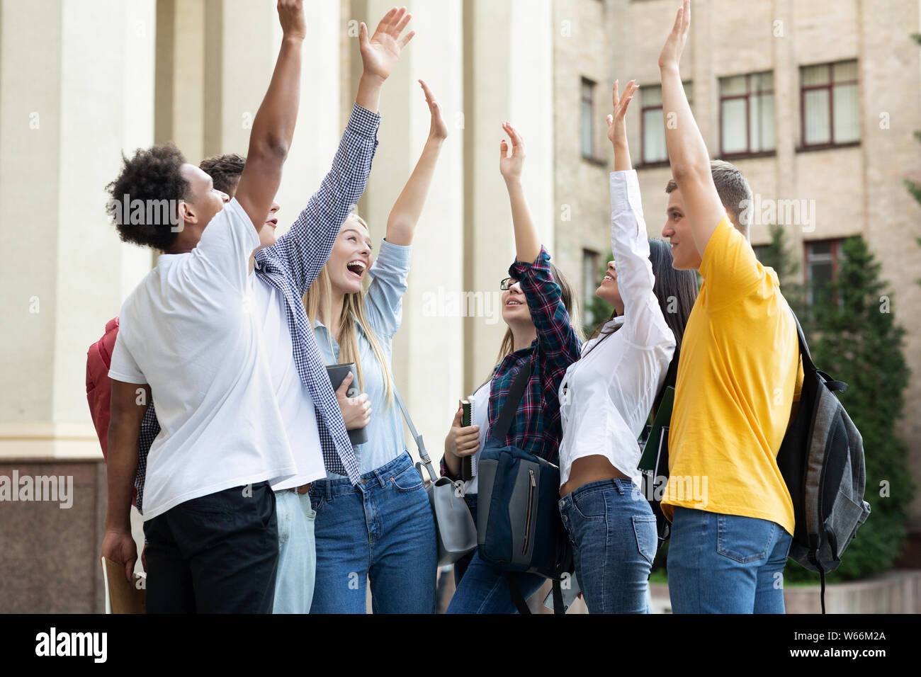 Happy students standing near university with raised hands Stock Photo