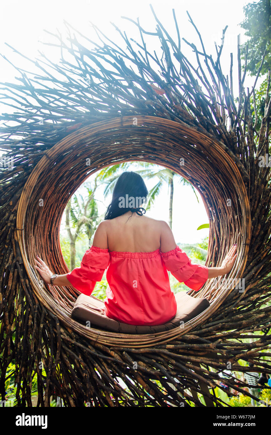 A female tourist is sitting on a large bird nest on a tree at Bali