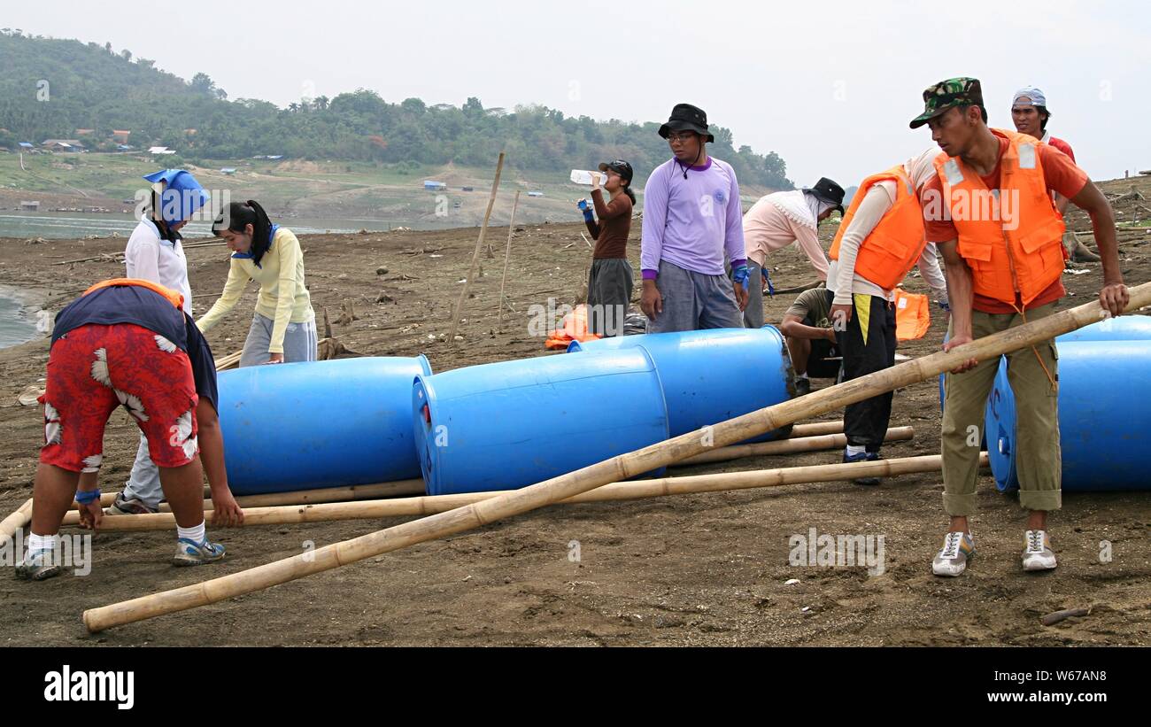 A group of young people work together to make an emergency boat using plastic barrel, bamboo sticks and ropes. Stock Photo