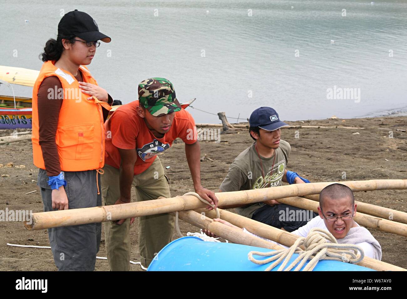 A group of young people work together to make an emergency boat using plastic barrel, bamboo sticks and ropes. Stock Photo