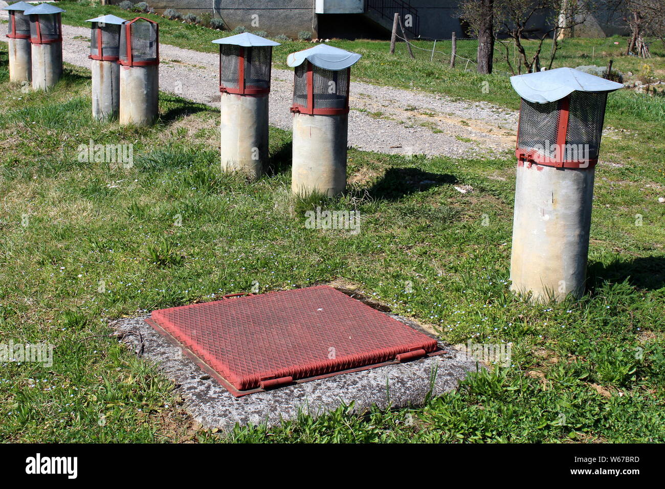 Closed strong manhole cover surrounded with multiple old concrete ventilation pipes covered with