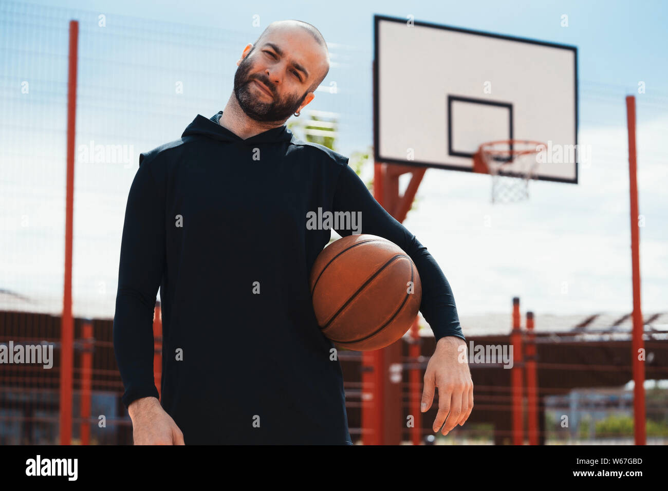 Attractive man on basketball court on basketball hoop and board background. Man is on focus and foreground, background is blurred. Stock Photo