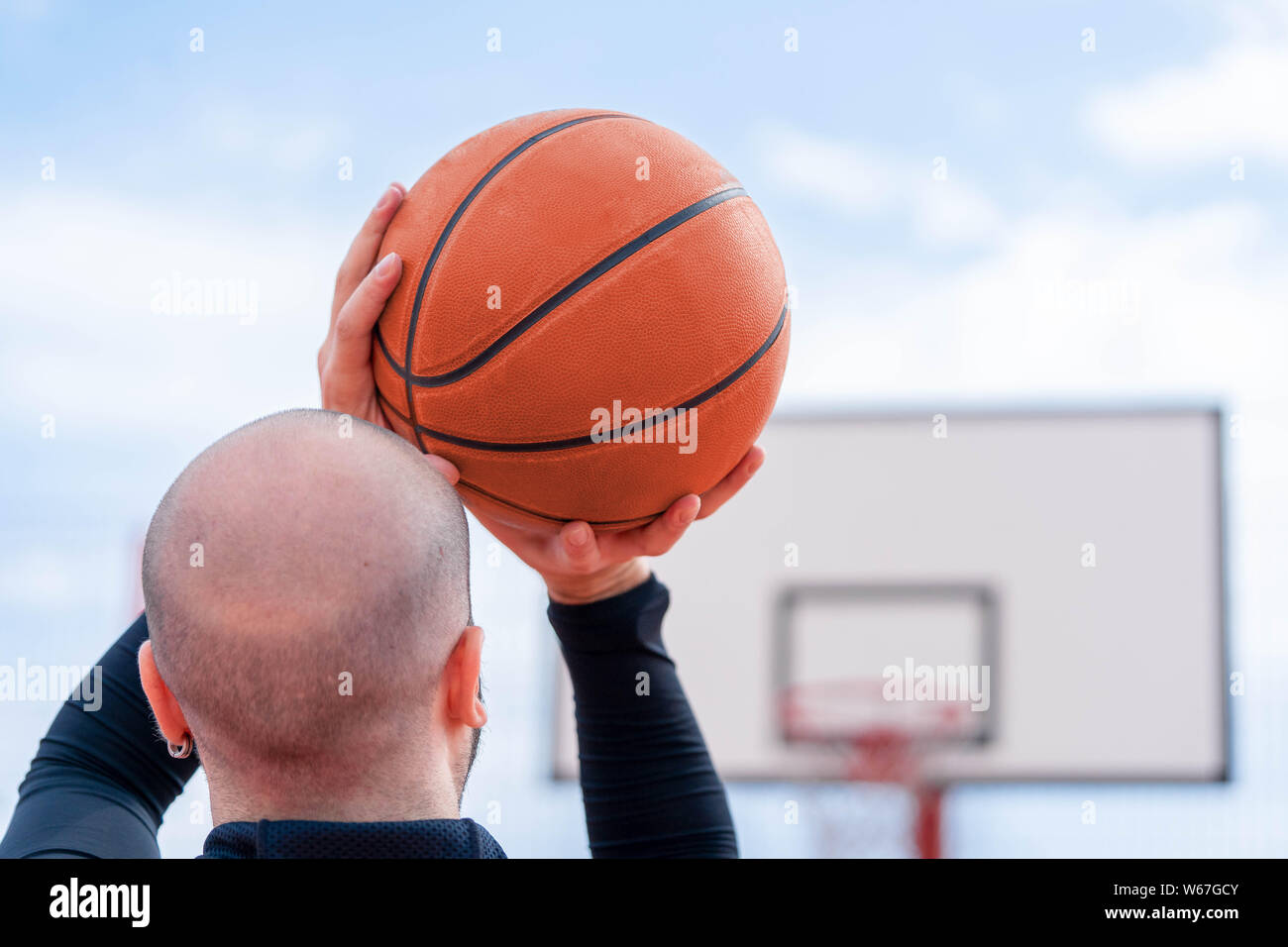 Close up of attractive man playing basketball on the basketball court. Man is on focus and foreground, background and hoop is blurred. Stock Photo