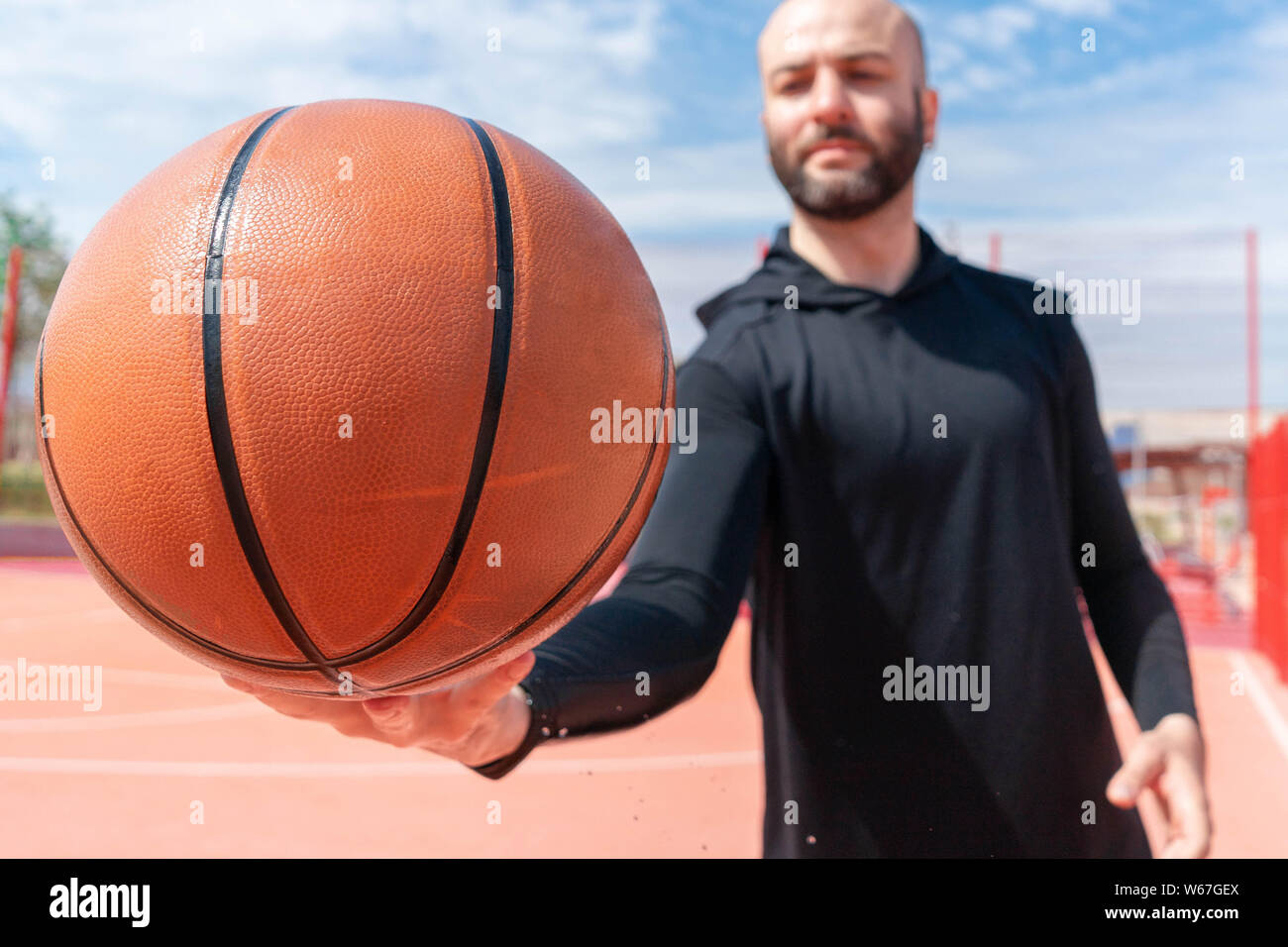 Close up of attractive man holding basket ball. Ball is on focus and foreground. Training outdoor Stock Photo