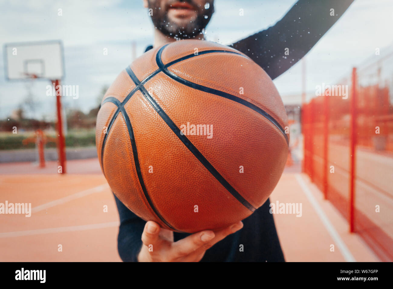 Close up of attractive man holding basket ball. Ball is on focus and foreground. Training outdoor Stock Photo