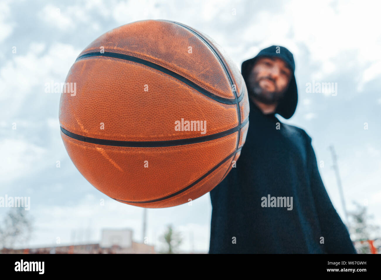 Close up of attractive man holding basket ball. Ball is on focus and foreground. Training outdoor Stock Photo