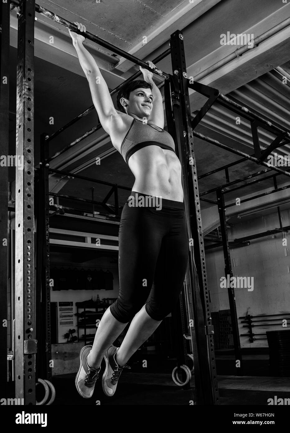 A young attractive woman with abs is doing toes to bar at the horizontal bar. The short haired sporty athlete is doing a functional fitness training. Stock Photo