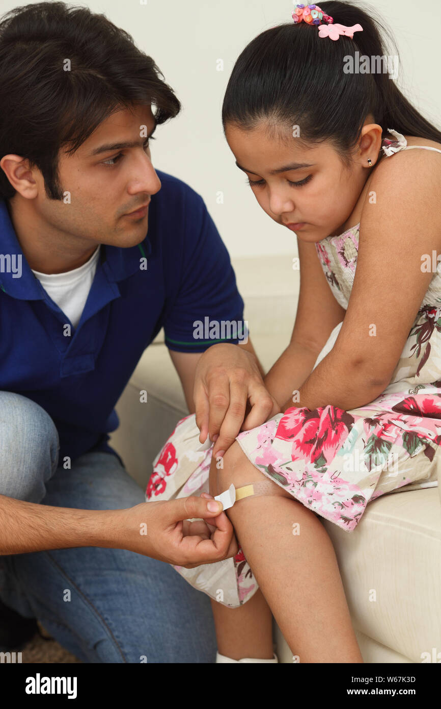 Man putting bandage on daughter,s knee Stock Photo